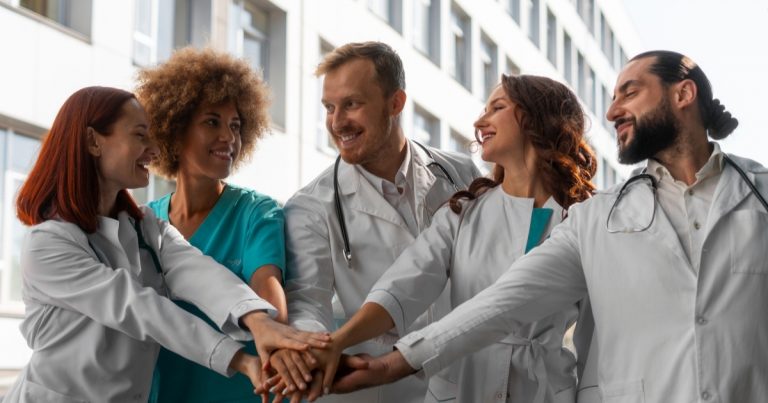 Grupo de médicos e enfermeiros juntando as mão ao centro em forma de união.
